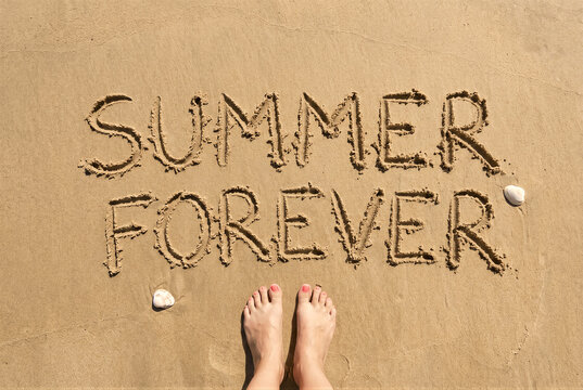 Top view of female feet on the sand with the words summer forever written in the sand, summer vacation concept