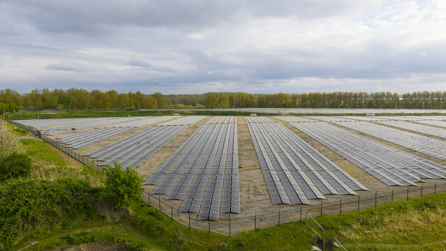 Aerial view of Zonnepark Braambergen solar farm featuring rows of photovoltaic panels surrounded by lush green trees and fields under a cloudy sky in Almere, Flevoland, Netherlands.
