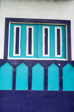 Ventana decorativa turquesa con marcos morados en fachada de estilo colonial