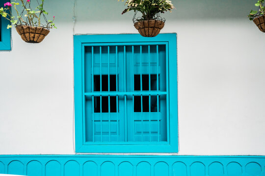 Ventana colonial turquesa con rejas y macetas colgantes en fachada blanca