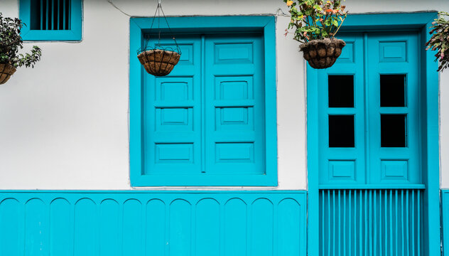 Fachada colonial color turquesa con puerta, ventana y macetas colgantes decorativas