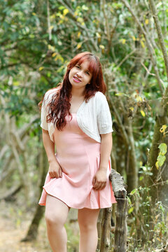 Mujer joven y bonita, sosteniendo su vestido mientras camina por un espacio abierto rodeado de naturaleza al aire libre. Chica linda con un vestido corto rosado y una chaqueta blanca.