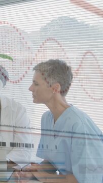 Vertical video: Nurse reviewing chart after doctor pointing tablet, causing red waveform on blinds