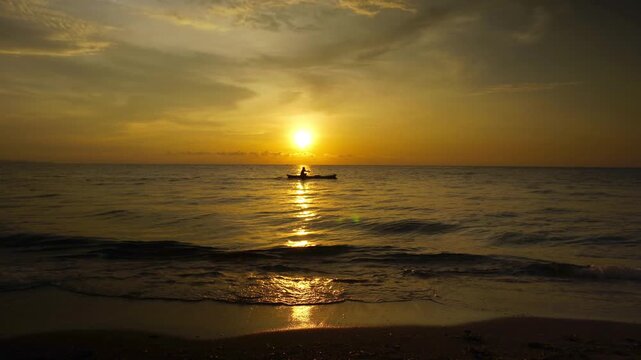 silhouette of Fisherman on Traditional Boat at Golden Sunset Over Tropical Ocean with Sun Reflection