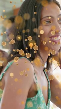 Vertical video: Woman replying to offscreen friend in cafe smiling, laughing through gold hex bokeh