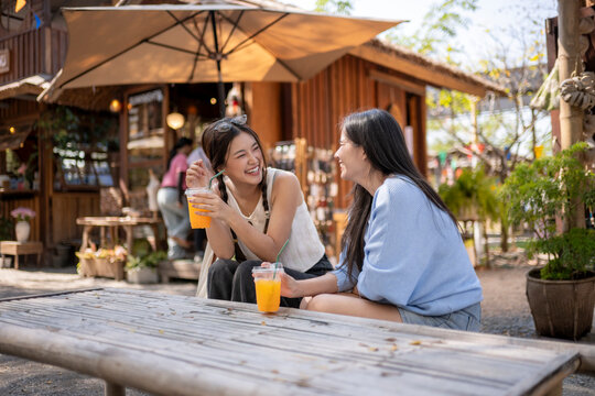 Asian friends laughing and drinking orange juice at outdoor cafe