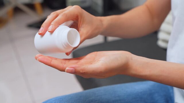 Woman sitting on sofa taking medication from a pill bottle at home, healthcare and treatment concept