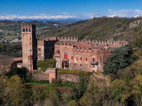 Aerial view of the historic Castello di Camino with its medieval brick tower and crenelated walls set against the snow-capped Alps and rolling hills in Camino, Piemonte, Italy.