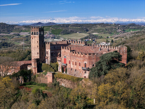 Aerial view of Castello di Camino with its tall brick tower and crenelated walls overlooking the Monferrato hills and snow-capped Alps Camino, Piemonte, Italy.