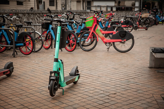 An electric rideshare scooter stands near parked shared bicycles in Bordeaux, france, illustrating urban micromobility, public rental transport and short distance travel in a city street setting.