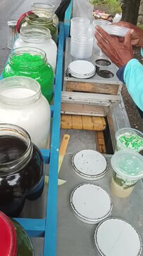 Street food vendor preparing fresh Indonesian iced cendol dessert in plastic cup.