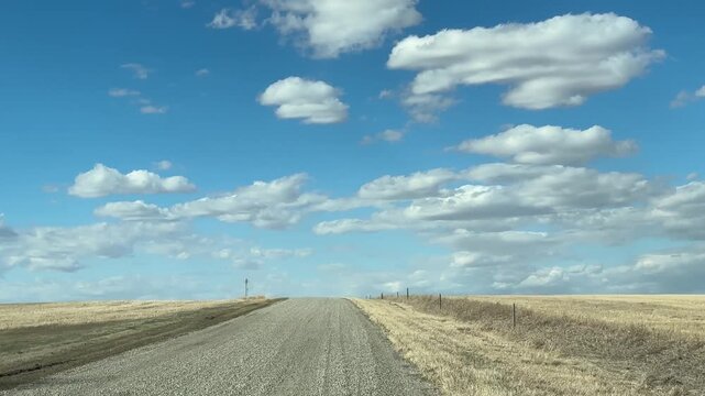 Driving on a rural gravel road through open prairie landscape under blue sky