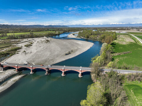 Aerial view of the red brick arched bridge crossing the Po river with a large gravel bank and snow-capped Alps in the background Verrua Savoia, Piedmont, Italy.