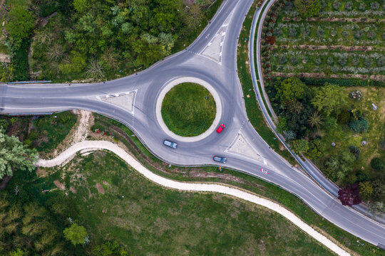 Aerial view of a traffic roundabout with cars driving through the intersection surrounded by lush green trees and fields in Reggello, Tuscany, Italy.