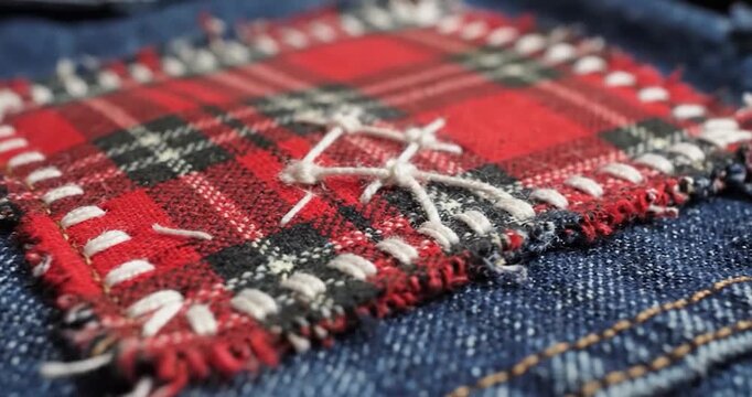 Close up of red plaid fabric patch hand stitched onto blue denim jeans