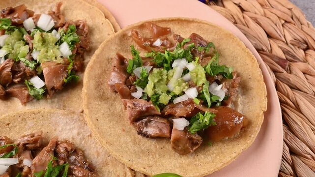 Aerial vew of slow-cooked carnitas tacos served with cilantro, onion, green salsa, and limes