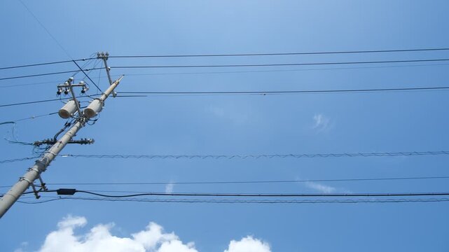 Parallel power lines against blue sky filmed from moving car, upward tracking utility wire footage