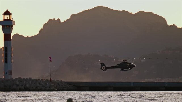 Helicopter lands on helipad near lighthouse at sunset calm sea mountain background cinematic motion.
