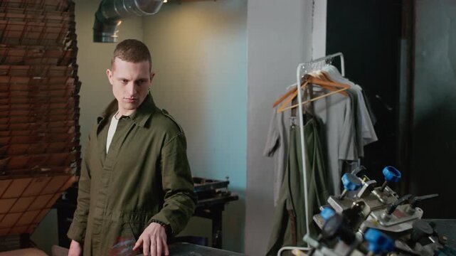 Medium slowmo shot of confident Caucasian male worker walking into screen printing and logo branding workshop while observing machinery and production equipment