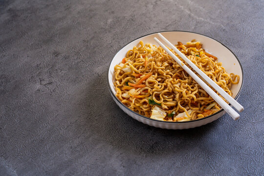 Javanese fried noodles or Bakmi Jawa with chopsticks served in a bowl on dark background, traditional Indonesian noodle dish with vegetables and savory flavor. Copy space