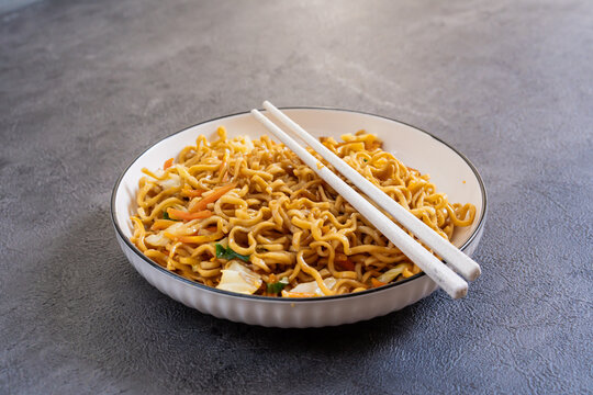 Javanese fried noodles or Bakmi Jawa with chopsticks served in a bowl on dark background, traditional Indonesian noodle dish with vegetables and savory flavor