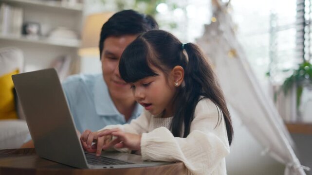 Asian father teaching daughter doing homework,online learning on laptop computer at home.Parents homeschooling and supporting girl during summer break.Concept of online education and online learning