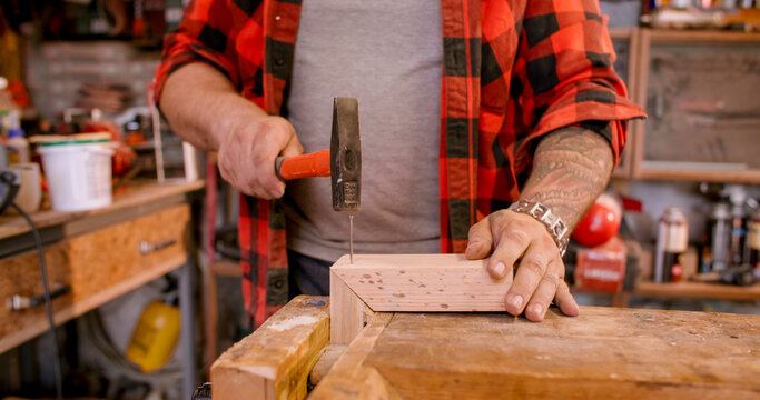 Joinery process. Woodworking hand tool. Male carpenter hand hammering nail into frame corner. Professional occupation at workbench.