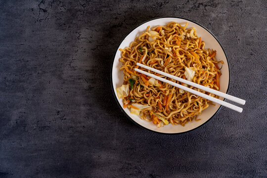 Javanese fried noodles or Bakmi Jawa with chopsticks served in a bowl on dark background, traditional Indonesian noodle dish with vegetables and savory flavor. Top View. Copy Space
