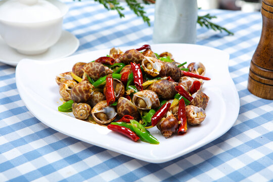 Spicy stir fried sea snails with chili peppers on white plate