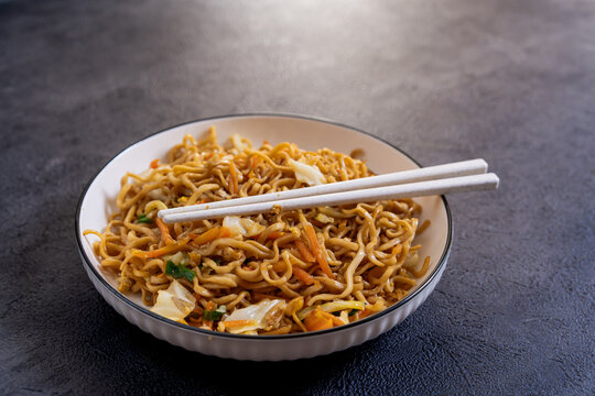 Javanese fried noodles or Bakmi Jawa with chopsticks served in a bowl on dark background, traditional Indonesian noodle dish with vegetables and savory flavor