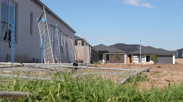 A residential construction site in a new housing estate in Tarneit, suburban Melbourne, Australia.&nbsp;Temporary fence and&nbsp;steel pipes scattered across bare dirt ground,&nbsp;modern homes&nbsp;in the background