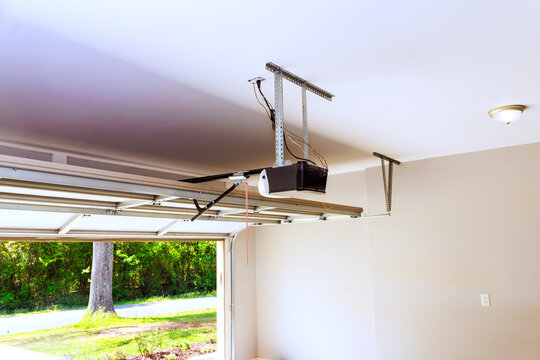 Garage door opener is mounted on ceiling, with door open, allowing to shine in.