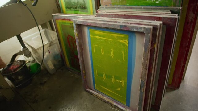 No people tilt up shot of many colorful screen printing frames arranged in rack and screen printing equipment inside creative workshop