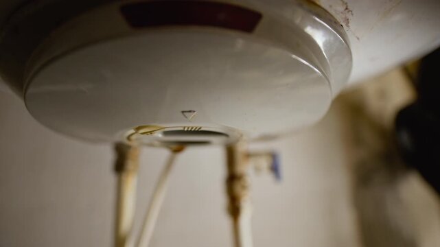 Extreme close up shot of water droplet forming and falling beneath plumbing fixture or pipe connection during household leak or maintenance problem