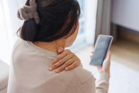 Woman suffering from neck pain while sitting on the couch at home, Health care and medical concept