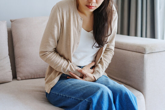 Young woman experienced stomach pain while sitting on the sofa at home, Health care and medical concept