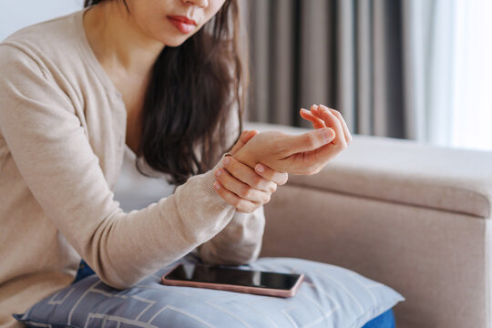 Woman suffering from wrist pain while using mobile phone at home, Health care and medical concept