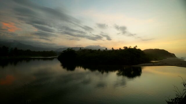 Cinematic view of the calm reflection at twilight in Los Naranjos, near Playa Los Angeles Cove in Santa Marta, Colombia. A serene tropical landscape at sunset with palm tree silhouettes