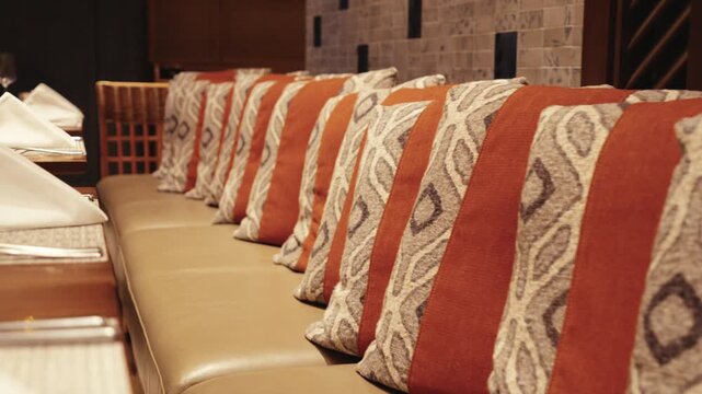 Row of decorative pillows with tribal motifs in terracotta and gray tones resting on a leather bench in a professional dining space.