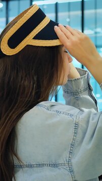 Trying straw visor hat in boutique caucasian woman experiments with brim placement, mirrorless styling moment, denim jacket shopper adjusts fit, playful curiosity under store lights