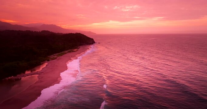 Vivid sunset view over Tayrona Los Naranjos coastline with breaking waves. Drone