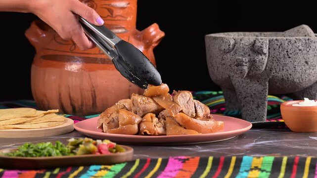 Woman's hand serving roasted pork carnitas with pork rind (cueritos). Authentic Mexican food