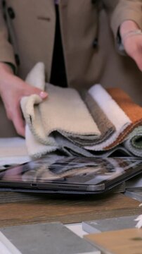Textile specialist feeling upholstery textures and comparing samples over tablet, hands smoothing boucle and velvet layers, testing softness and drape in cozy creative studio environment