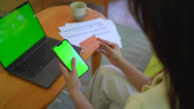Asian Indonesian woman holding credit card and smartphone with green screen