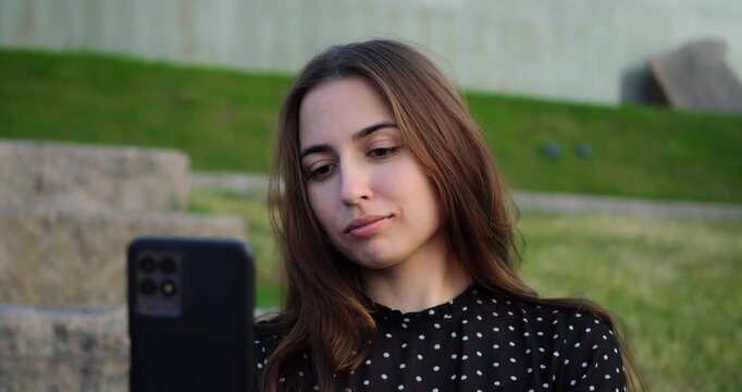 Lady taking selfportrait on park steps. Woman peacefully recording short social media video outdoors. Relaxed woman in casual attire capturing selfie for online content in park setting