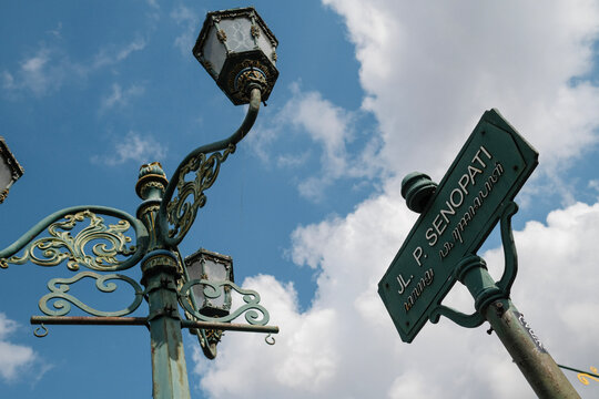 Javanese street sign and ornate street lamp against cloudy blue sky