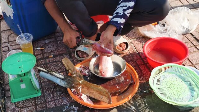 Local authentic and food culture manifest through traditional seafood preparation at street market. Vendor cleans fresh fish on block using manual tools. Local authentic style defines food culture.