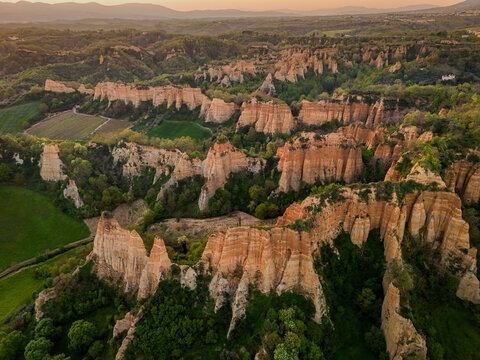 Aerial view of the unique clay cliffs of Le Balze del Valdarno surrounded by lush green vegetation and rolling hills during golden hour in Botriolo, Toscana, Italy.