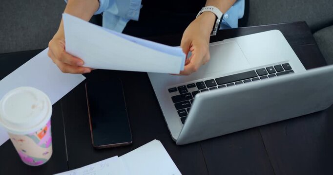 Organizing papers now. Arranging documents on workspace diligently. Sorting and annotating files at tidy desk station. Carefully managing paperwork alongside cup of coffee and electronic devices