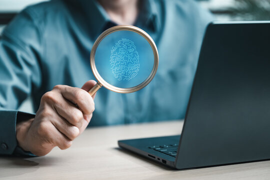 Hand holding magnifier showing digital fingerprint over laptop, representing biometric authentication, passwordless login, and advanced cybersecurity for identity protection.